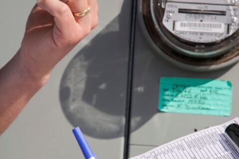 Person checking utility meter and recording readings on clipboard
