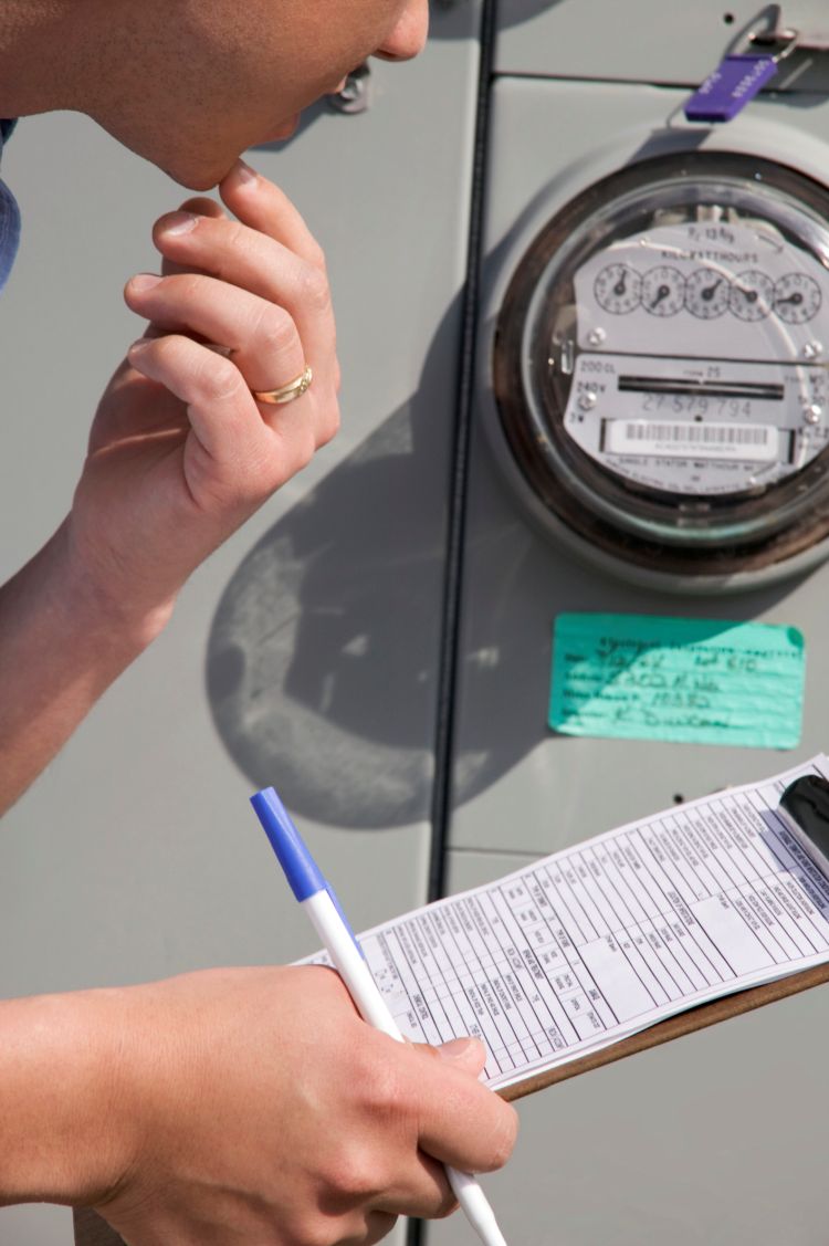 Person checking utility meter and recording readings on clipboard