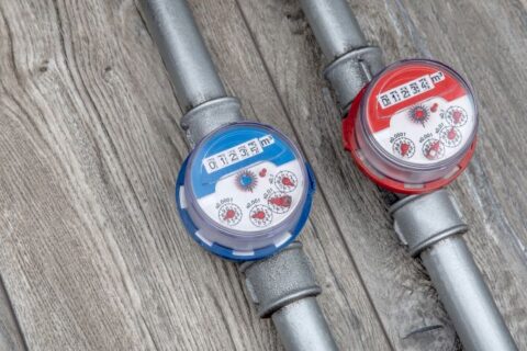 Two water meters on metal pipes showing usage readings on wooden surface