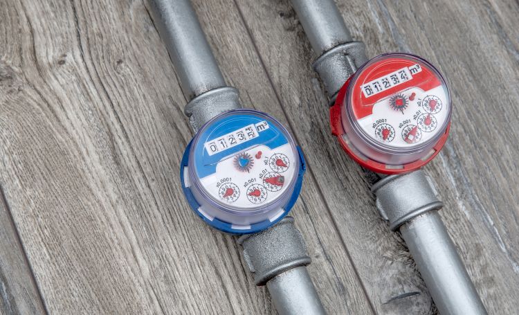Two water meters on metal pipes showing usage readings on wooden surface